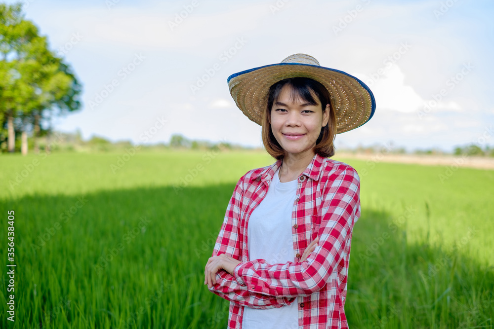 Asian farmer woman wear red shirt and hat stand with cross arm at green rice farm.