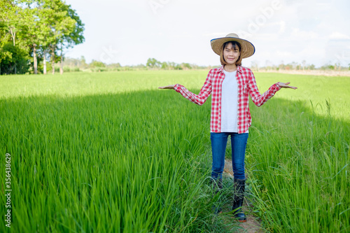 Asian farmer woman wear red shirt and hat stand with raise hand at green rice farm. © Thannaree