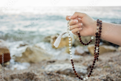 Woman hand holding japa mala. Mantra meditation technique by the sea. Hinduism and buddhism