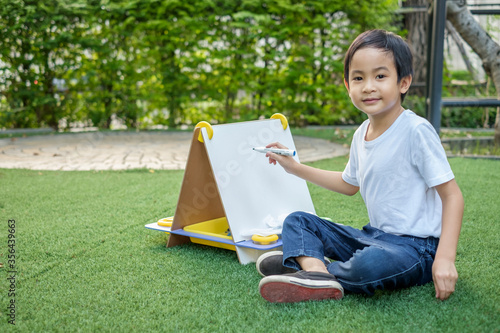 Happy asian boy wear white T-shirt and jean sitting drawing white board at home garden.