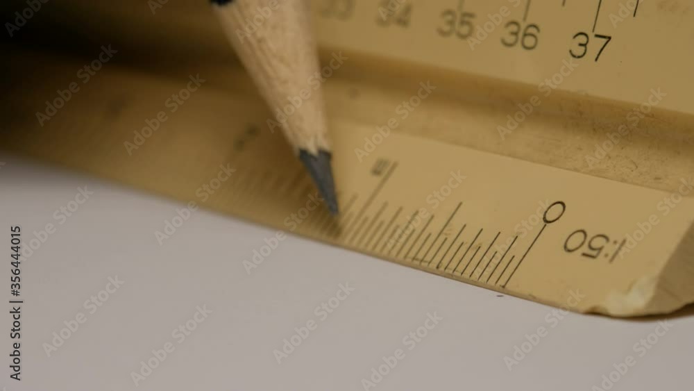 Close up of using a triangular scale ruler with pencil on white paper ...