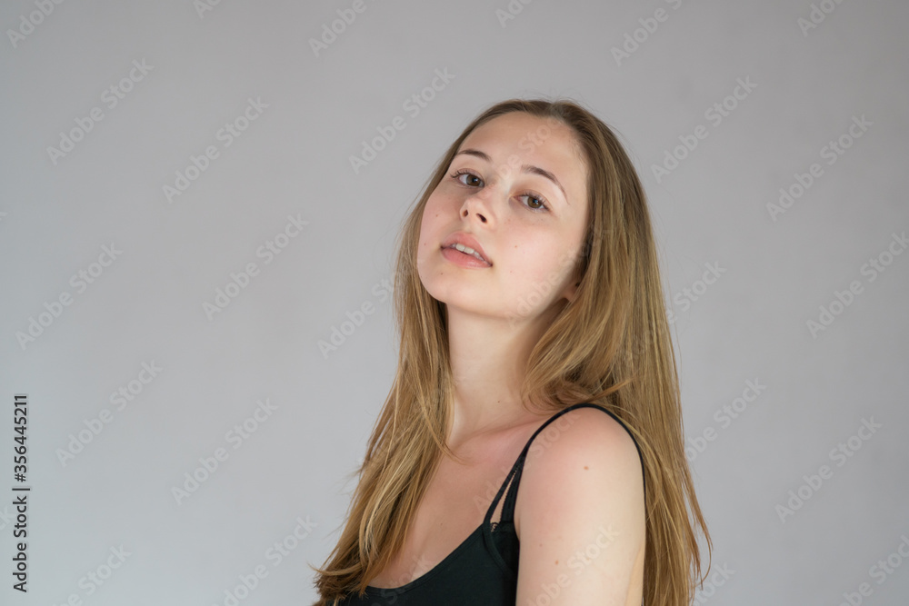Portrait of a languishing and charming young woman with long hair posing looking at the camera on a grey background Portrait of a languishing and charming young woman with long hair posing looking at the camera on a grey background