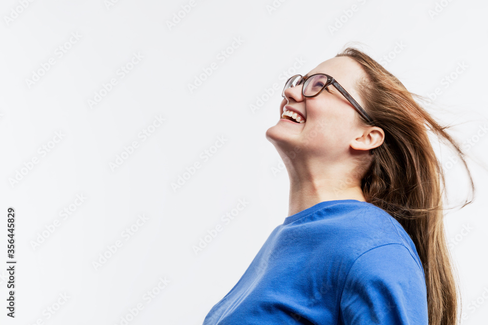 Laughing young girl with glasses in a blue t-shirt. Happiness and joy. White background. Space for text. Laughing young girl with glasses in a blue t-shirt. Happiness and joy. White background. Space for text.