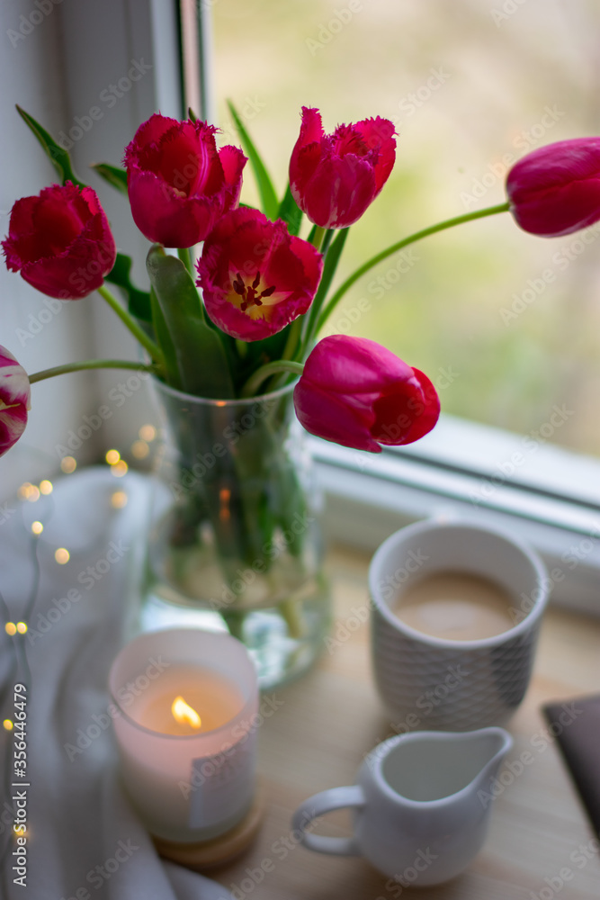 Still life coffee at home, a cozy coffee, tulips in a vase. Coffee on the windowsill, comfort at home. Milk jug  mug, candlestick, envelope and postcard on wooden desk. Spring content