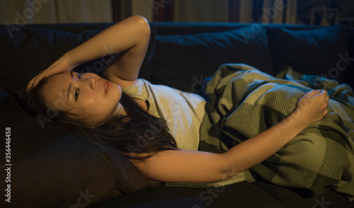 dramatic portrait of young beautiful sad and depressed Asian Korean woman lying in pain at living room sofa couch broken heart suffering depression and anxiety