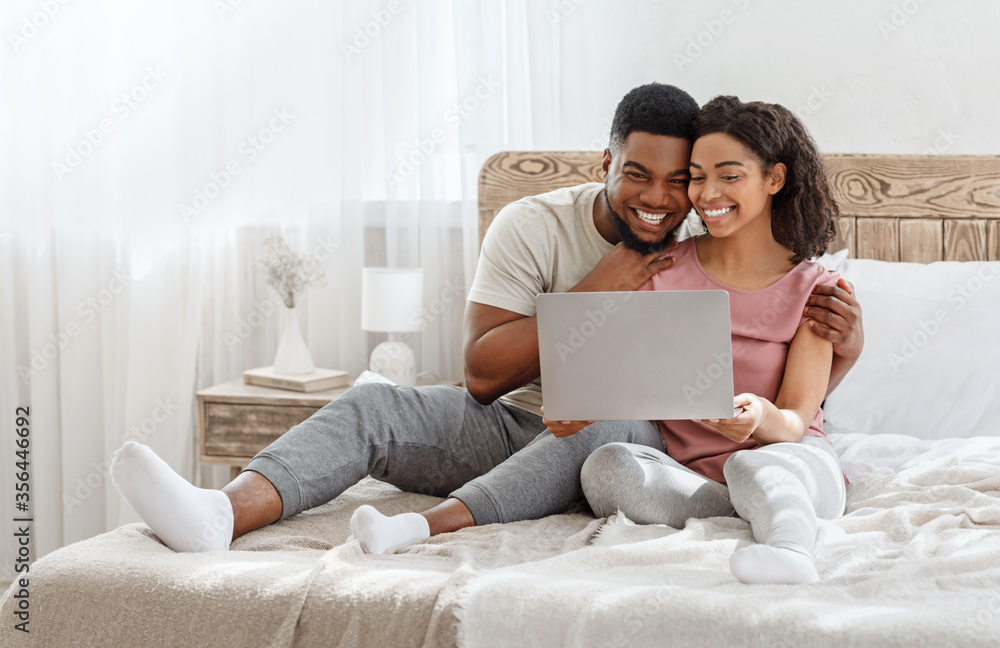 Couple in love watching photos on laptop in bedroom Couple in love watching photos on laptop in bedroom