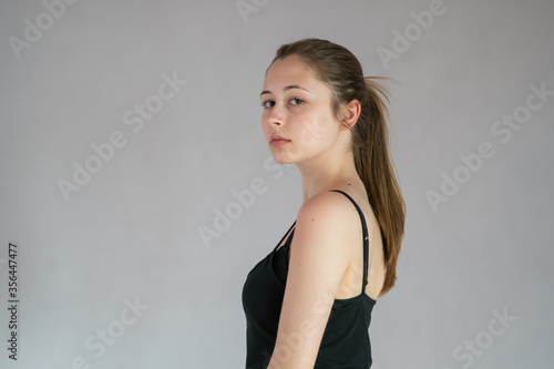 Semi profile portrait of a pretty teenage girl with ponytail hair posing looking at the camera against a grey background
