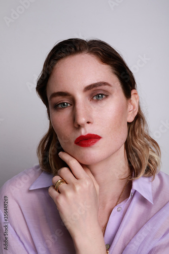 Portrait of young stunning model with impressive red lips. Studio photo shoot of pretty woman in purple fashionable shirt.