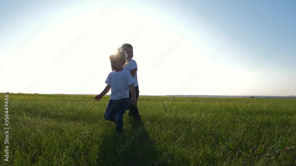 Two children in white t-shirts running on green fresh grass. Happy children enjoy life. The concept of teamwork. Two children in white t-shirts running on green fresh grass. Happy children enjoy life. The concept of teamwork.