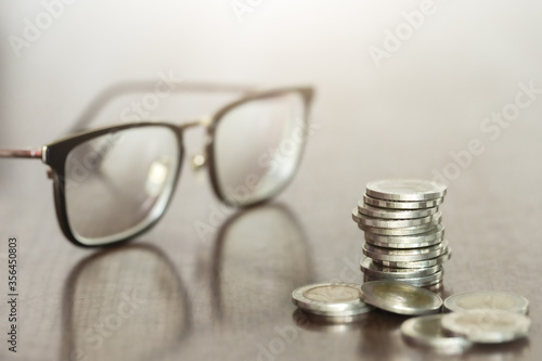 Close-up rows of money coins with a blurred glasses on the desk background