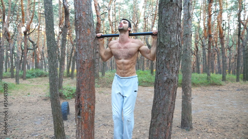 Athletic man showing some abdominal exercises on horizontal bar. Muscular guy working out at forest. Sportsman training outdoor. Concept of sport and active lifestyle. Slow motion Dolly shot
