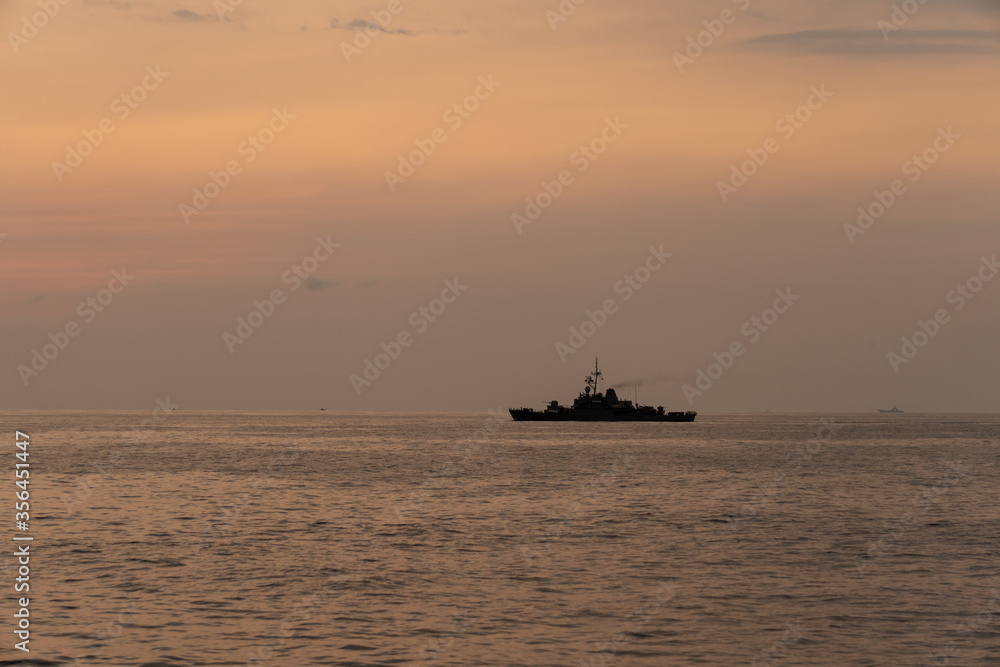 Silhouette of a warship sails along the trade route to protect national resources from illegal activities at sea when the evening before sunset.