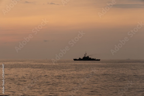 Silhouette of a warship sails along the trade route to protect national resources from illegal activities at sea when the evening before sunset. © Kamchai