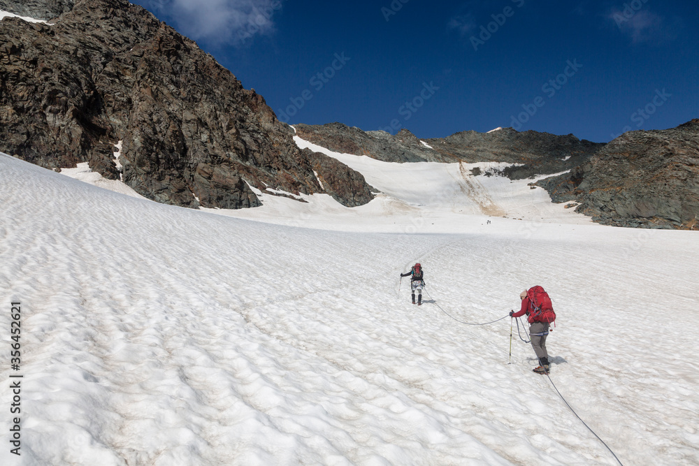 Climbers team on a trail through a dangerous glacier and avalanches in Austiran Alps. Route to the Grossglockner rock summit, Austria