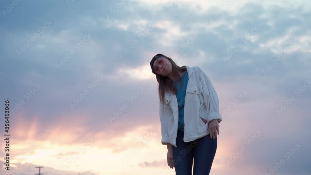 Young beautiful woman dancing at sunset. Warm day and soft backlight. Pretty girl in cap relaxing during summer vacation.
