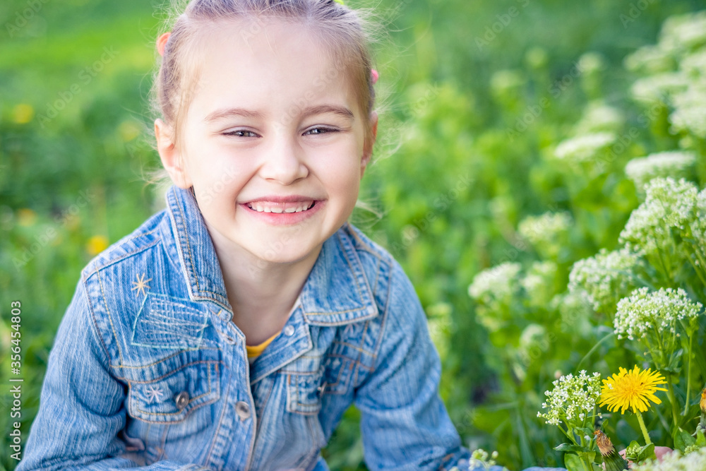 Smiling attractive preteen girl sitting near grass and flowers in jeans jacket Smiling attractive preteen girl sitting near grass and flowers in jeans jacket