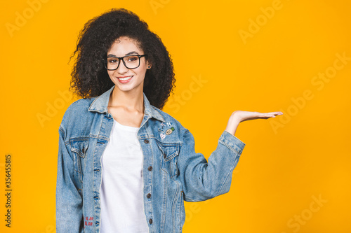 Portrait of a happy young african american curly woman pointing fingers away at copy space isolated over yellow background. photo