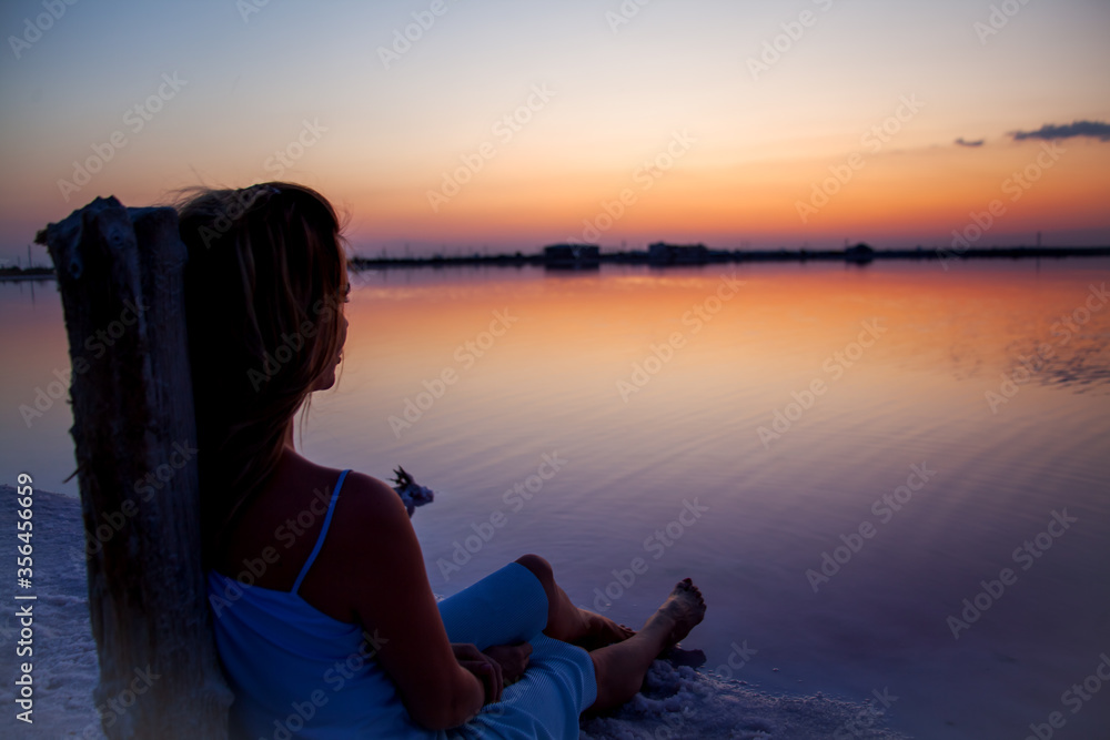 Rear view of the woman back silhouette look to the purple sunrise in water on summer. Woman sit on the shore of the salt beach at pink lake. vacation lifestyle near ocean Rear view of the woman back silhouette look to the purple sunrise in water on summer. Woman sit on the shore of the salt beach at pink lake. vacation lifestyle near ocean