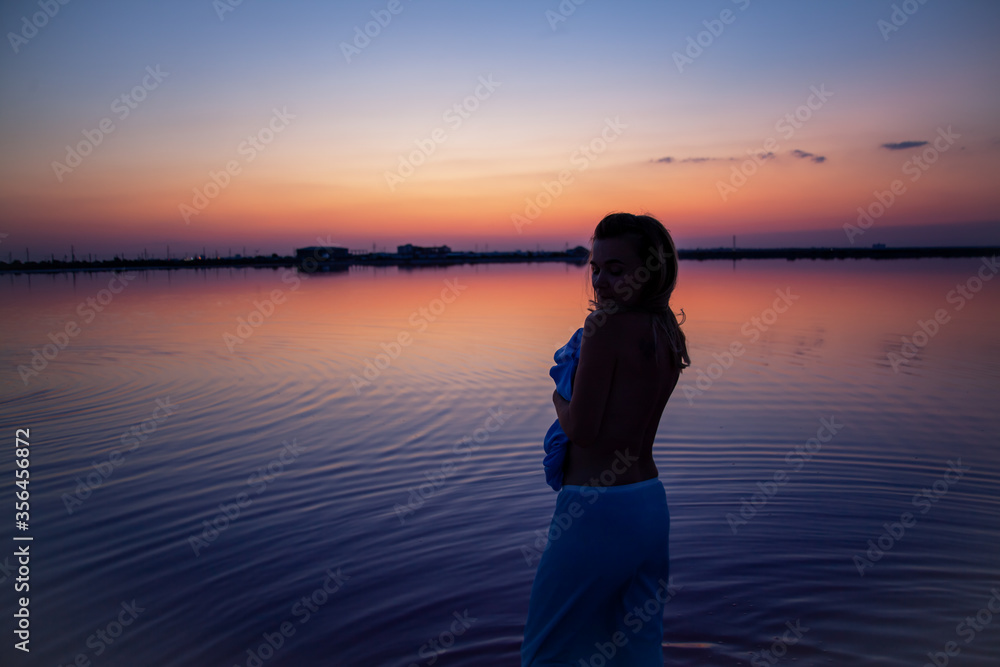 Rear view of the woman back silhouette look to the purple sunrise in water on summer. Woman sit on the shore of the salt beach at pink lake. vacation lifestyle near ocean