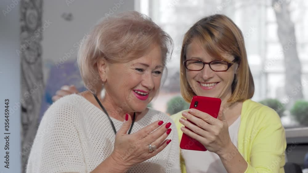 Mature woman showing something on her smart phone to her senior mother. Elderly mother and her adult daughter using smart phone together. Online, family concept Mature woman showing something on her smart phone to her senior mother. Elderly mother and her adult daughter using smart phone together. Online, family concept