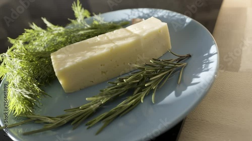 Close up of cheese and greenery on a glass plate. Stock footage. Delicious cheese with fresh green dill and rosemary, food and french ciusine concept. photo