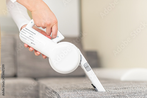 Woman vacuuming furniture in a house with a hand-held portable vacuum cleaner.