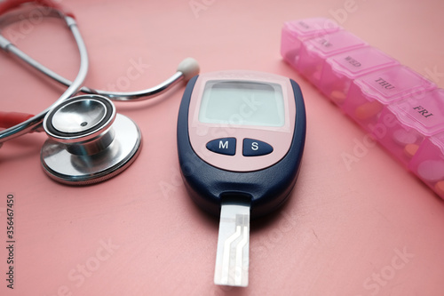 Blood glucose meters, stethoscope and pill box on pink 