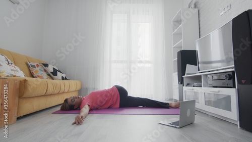 Androgynous Transgender beautiful young gay man doing spine stretching exercises. On-line home work out man using internet services with help of her instructor on laptop