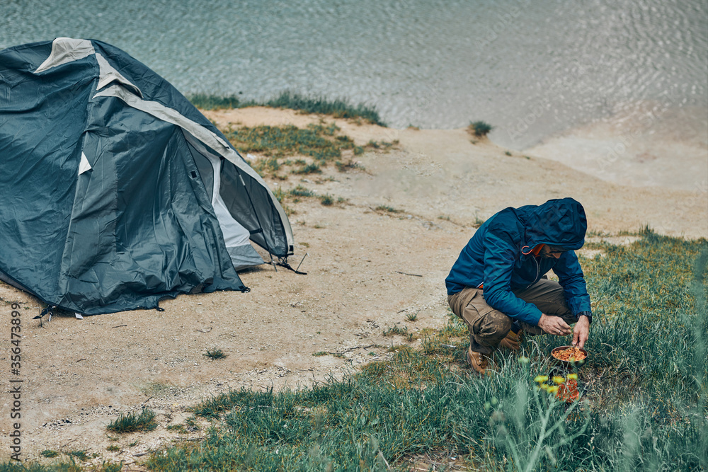 Young attractive bearded man preparing lunch on camping trip. Weekend activities concept. Young attractive bearded man preparing lunch on camping trip. Weekend activities concept.
