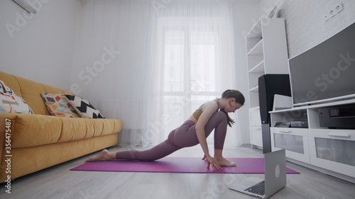 On-line work out woman using internet services with help of her instructor. Portrait of a beautiful slim sporty woman practicing yoga on a mat. Woman doing stretching exercises on violet mat