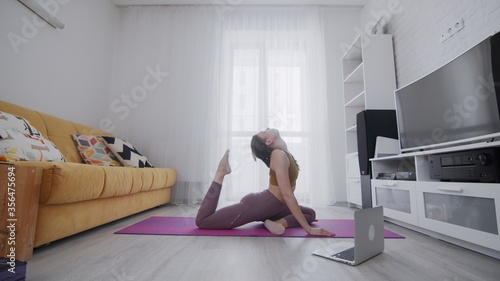 On-line work out woman using internet services with help of her instructor. Portrait of a beautiful slim sporty woman practicing yoga on a mat. Woman touches head with her foot