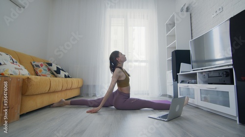 Portrait of a beautiful slim sporty woman practicing yoga on a mat. Woman in activewear doing splits exercise on violet mat at home