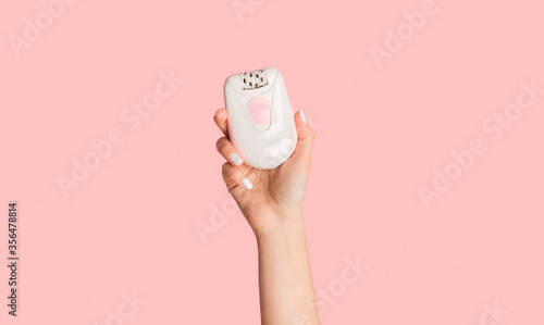 Unrecognizable millennial girl showing modern electric epilator on pink background photo