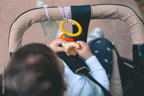 Tableau sur toile One year old baby sitting in stroller and eating white brad