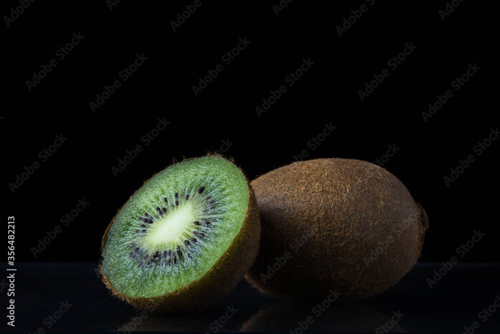 Obraz premium Two kiwi on a black background. One kiwi is whole, the other is cut in half. exotic fruit.