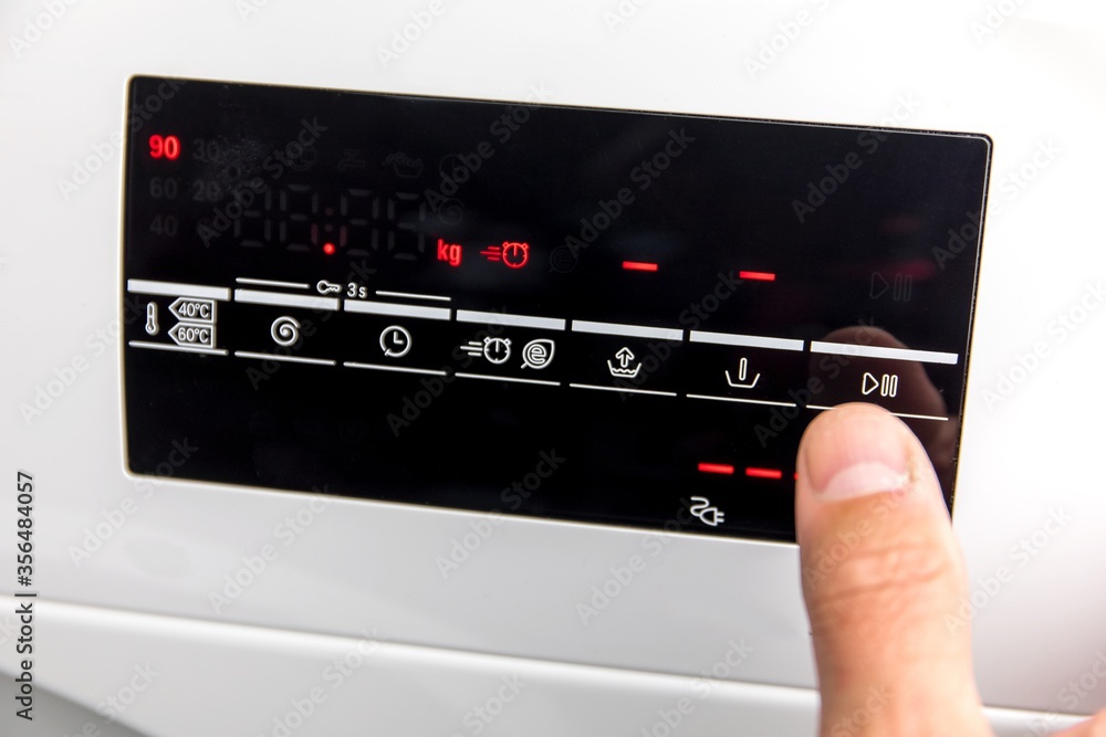 Close Up Of Man Choosing Cycle Program On Washing Machine. Adjusting wash settings on the control panel of washing machine. Smart home concept. Close Up Of Man Choosing Cycle Program On Washing Machine. Adjusting wash settings on the control panel of washing machine. Smart home concept.