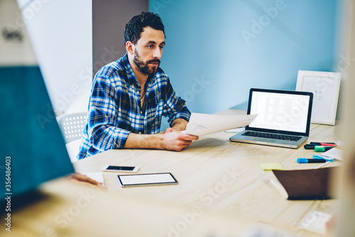 Male employee holding finance report and researches in coworking space