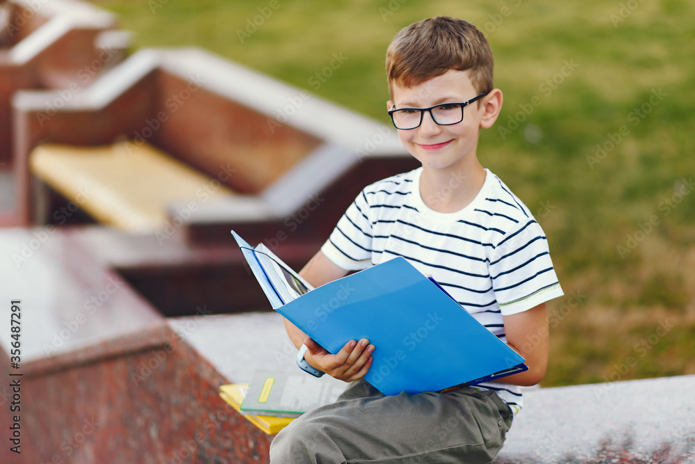 Fototapeta premium Pupil near school. Boy sitting with a folder.