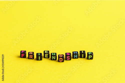 The word friendship composed from cubes with multicolored letters on a yellow background. A close-up.