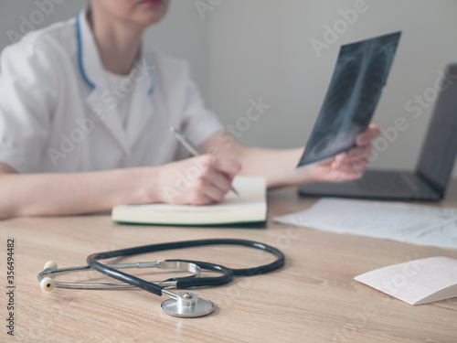 Doctor working with laptop computer and writing on paperwork. Hospital background.