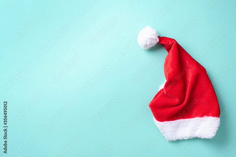 Red Santa Claus hat on blue background. Top view. Copy space. Advent time. New year composition. Decoration for winter holidays celebration. Christmas greeting card Red Santa Claus hat on blue background. Top view. Copy space. Advent time. New year composition. Decoration for winter holidays celebration. Christmas greeting card