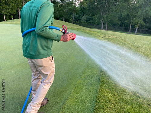 Vászonkép Water is sprayed on a golf green by a maintenance worker