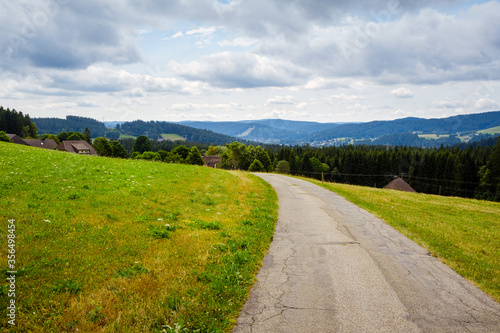 picturesque panorama with deserted road between sloping meadows in the High Black Forest landscape in Breitnau, Baden-Württemberg, Germany on a cloudy day in summer