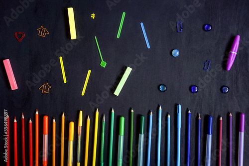 Colorful stationery on black. Flat lay. Row of tools  gradient rainbow colors.