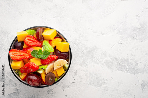 Fruit salad with mango, strawberries, kiwi, peach in a bowl top view with copy space