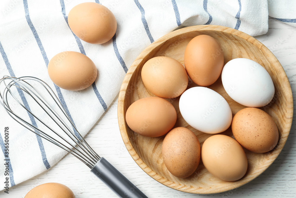 Chicken eggs and whisk on white wooden table, flat lay Chicken eggs and whisk on white wooden table, flat lay