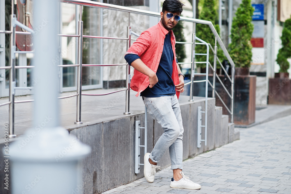 Portrait of young stylish indian man model pose in street in sunglasses.