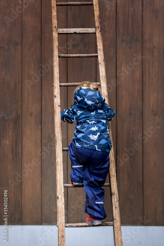 Child confidently steps on wooden step ladder. Courageous child climbs up. Kind tritt selbstbewusst auf hölzerner Trittleiter. Mutiges Kind klettert nach oben. photo