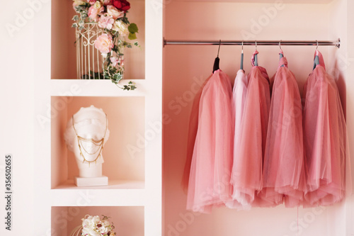Dressing closet with pink clothes is arranged on hangers. The wardrobe is full of pink skirts, accessories on the shelves.
