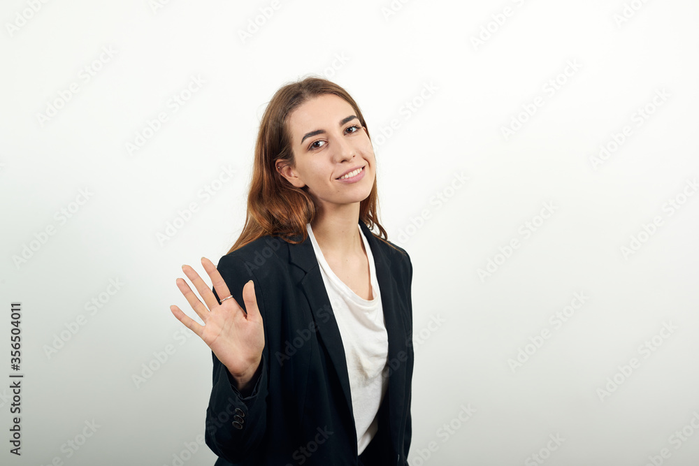 Hello arm sign, showing the five fingers, waving and greeting with hand as notices someone. Young attractive woman with brown hair in a light t-shirt, black jacket on white background Hello arm sign, showing the five fingers, waving and greeting with hand as notices someone. Young attractive woman with brown hair in a light t-shirt, black jacket on white background